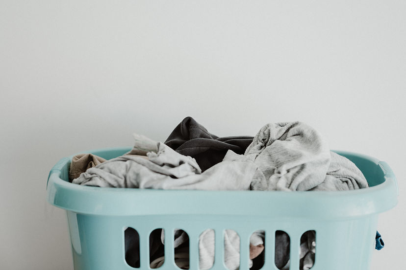 A light blue laundry basket brimming with crumpled clothes in neutral tones against a plain white background
