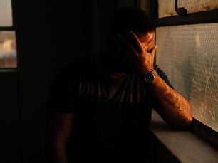 Person sitting in low light with hand covering face, reflecting emotional pain and the lasting impact of narcissistic parenting