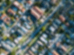 Aerial view of a suburban neighborhood with rows of houses, green lawns, and tree-lined streets under clear skies.
