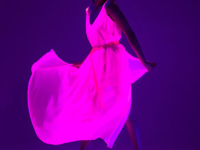 Woman in glowing pink dress poses under ultraviolet light, creating a dramatic effect against a dark purple background.