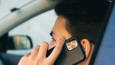 A man in a car speaks on the phone; phone systems powered by AI can help customers set dealership service and sales appointments.