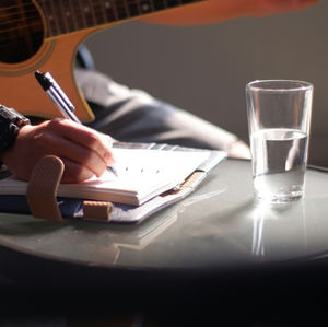 Close-up of a hand strumming an acoustic guitar with a pencil-like pick, warm blurred background, focused and calm