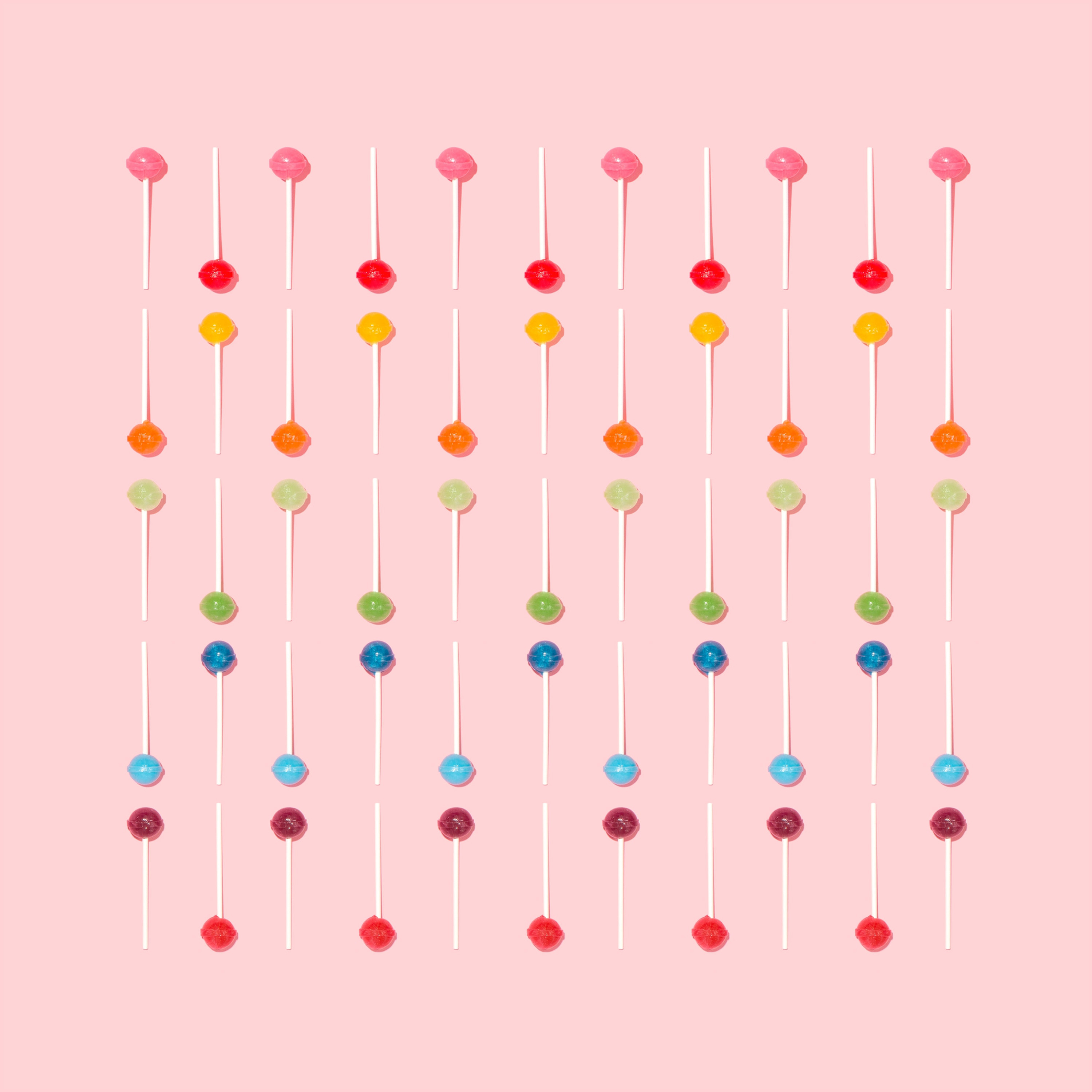 A stock image of multi-colored lollipops, with one row for each color of the candy, and the sucker candies are alternating positions in each row as they are tiled down the photo.