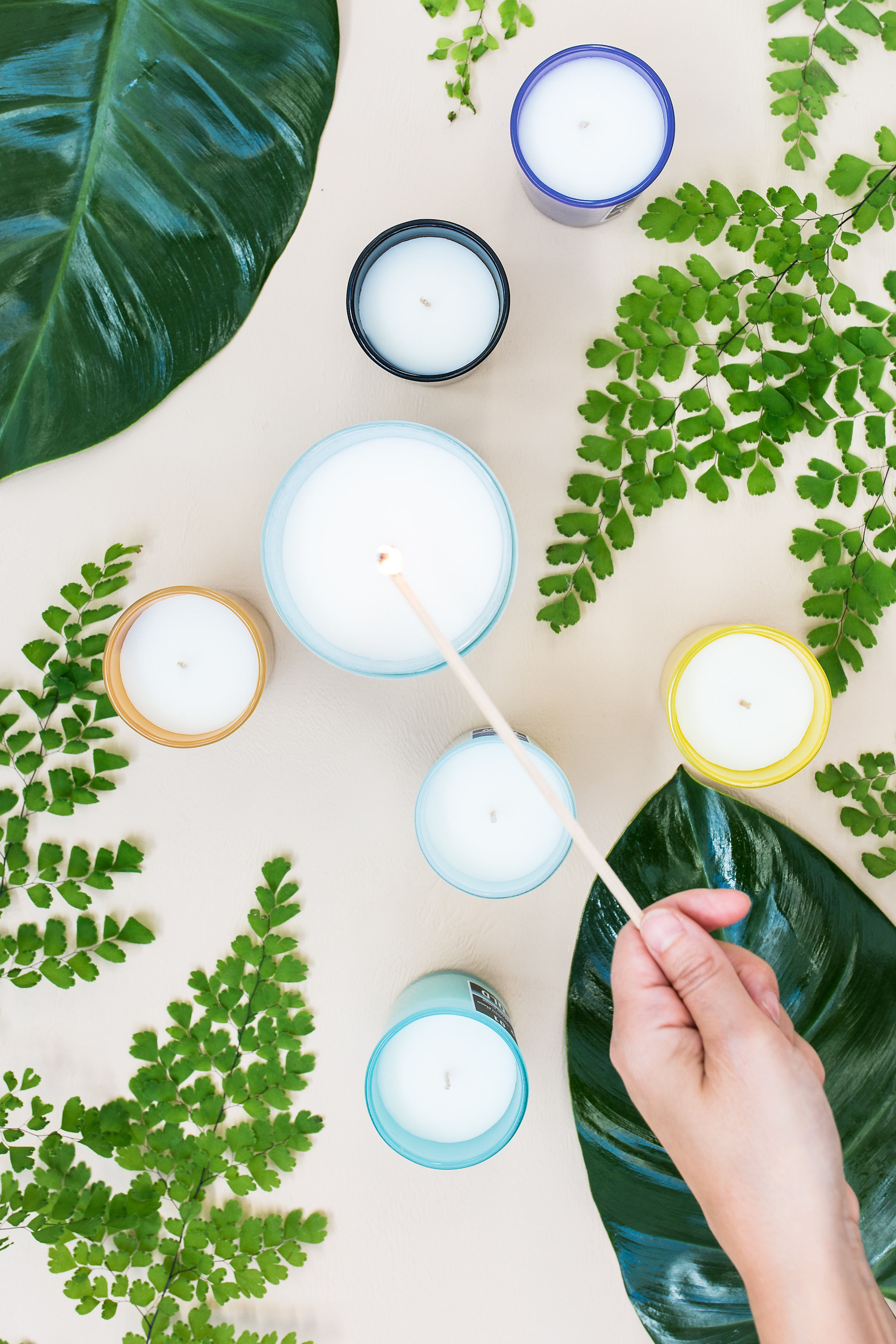 Hand lighting colorful candles surrounded by greenery