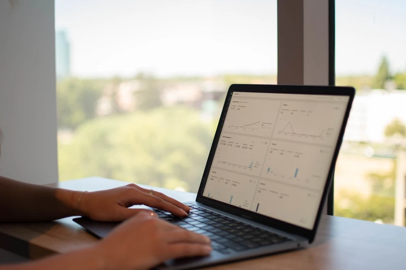Person typing on a laptop beside a bright window, with notes on the screen