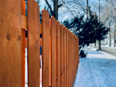 Wooden picket fence along a snowy sidewalk in winter