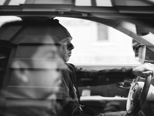 Black and white photo of two people driving in the front seat of a car.