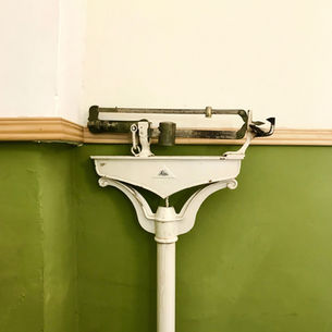 Vintage white Seca beam scale against a green-and-cream wall, with rusted weights and ruler markings.