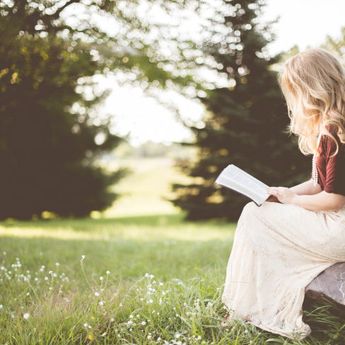woman reading book on rock in field
