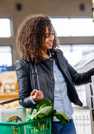 woman wearing a black jacket and blue shirt in a supermarket buying goods holding a shopping basket