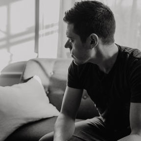 Man sitting alone on a couch with hands on knees, looking away in deep reflection, symbolizing guilt and emotional healing after a relationship.