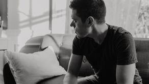 Man sitting alone on a couch with hands on knees, looking away in deep reflection, symbolizing guilt and emotional healing after a relationship.