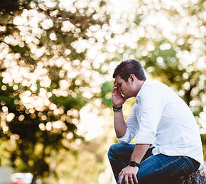 Married man sitting outdoors at sunset with his head resting in his hand