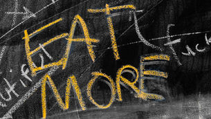 yellow chalk on a blackboard saying "EAT MORE"