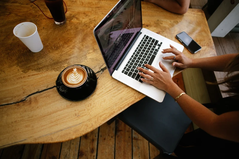 woman typing on a laptop drinking a hot latte in a cafe updating her website