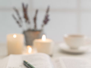 Open book with a green pen on its pages, lit candles and a mug softly blurred in the background, creating a calm study mood.
