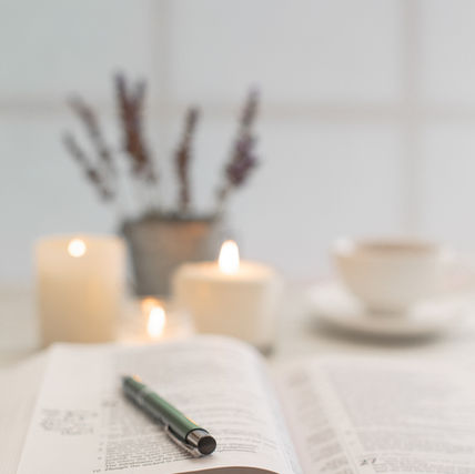An open Bible on a wooden surface with soft candlelight and lavender in the background, set up for quiet study time.