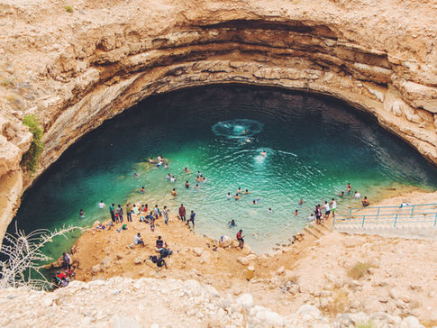 Travelers and locals play and swim in the dark turquoise waters of the Bimmah Sinkhole in Oman.