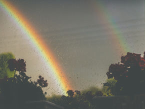 View from a window of a rainbow peeking through grey skies