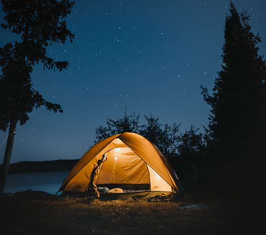 Yellow tent with a light on in under the starry sky next to a lake