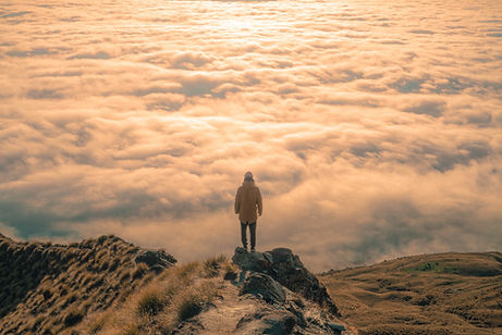 Person standing on mountain alone looking out over clouds