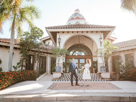 Couple holding hands in front of an elegant venue entrance with arched doorway and Spanish-style architecture