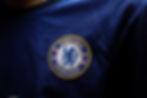 Close-up of a blue Chelsea FC jersey with a zigzag pattern. The club badge shows a lion holding a staff, encircled by "Chelsea Football Club."