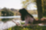 A woman with long hair reading by a river