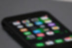 Smartphone close-up showing colorful app icons on the screen, including Photos, Maps, and Weather, on a gray surface.
