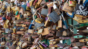 Colorful padlocks crowded on a bridge railing, many with names and dates written on them, creating a dense, romantic display.