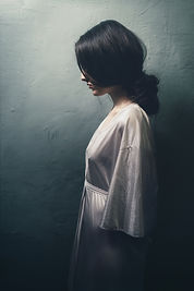 Side view of a woman with dark hair standing wearing a white silky night gown