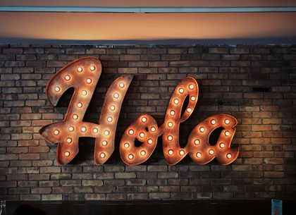 Metal sign displaying 'Hola' on a brick wall
