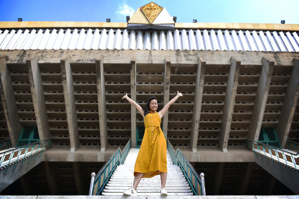 A confident looking woman standing on a staircase with her arms stretched toward the sky and a smile on her face.
