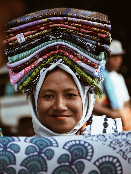 A smiling lady carrying bunch of clotes on her head in Lombok