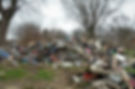 A large pile of assorted debris, including wood, fabric, and trash, sits in a grassy area