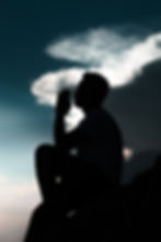 the silhouette of a man praying, sitting on a rock with a moody sunset background.