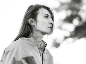Black-and-white portrait of a woman in a zip-up jacket, looking upward outdoors with a thoughtful, calm expression.