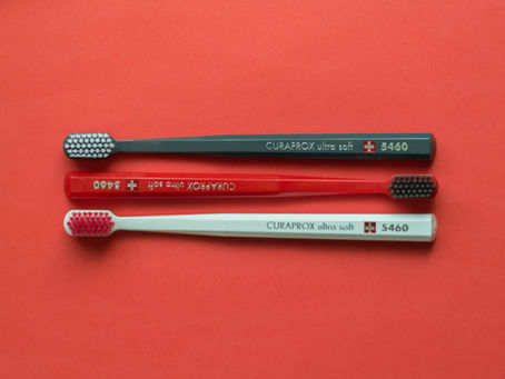 Three CURAPROX toothbrushes in gray, red, and white on a red background, featuring the text "ultra soft" and "5460."