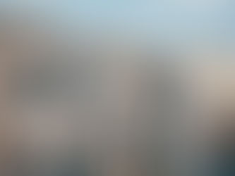 Stone buildings with closed balconies line a narrow street in a historic city. Blue shutters add color under a partly cloudy sky.
