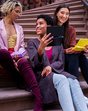 Three college students are sitting on steps, smiling and talking.