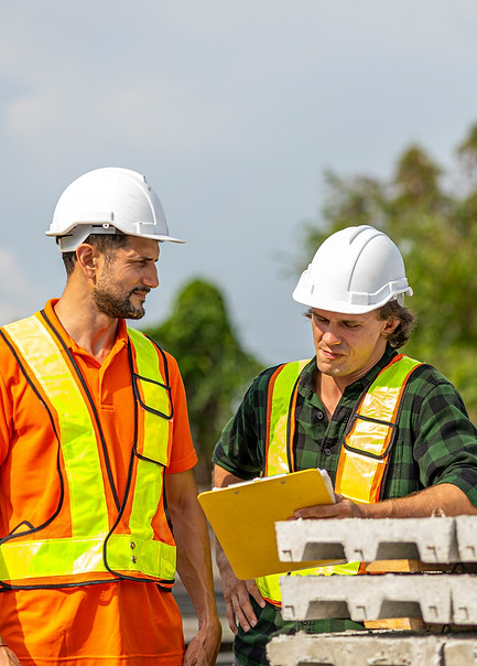 Two construction workers in hard hats reviewing documents at a job site