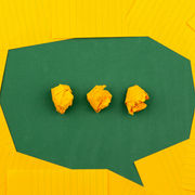 Yellow crumpled papers on a green background shaped like a speech bubble, surrounded by flat yellow lined papers. Bright and creative mood.