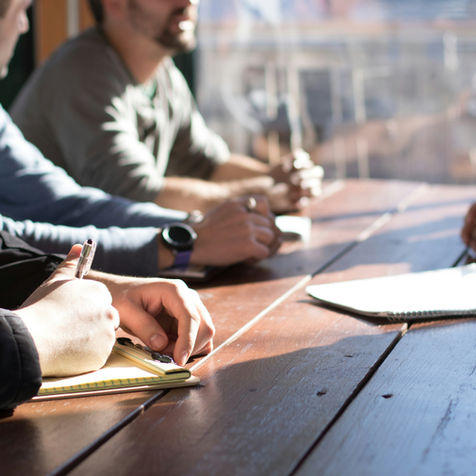 People taking notes at a wooden table during a meeting