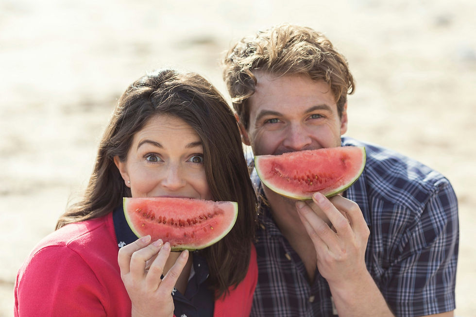 A couple holding watermelon slices like smiles on a beach.