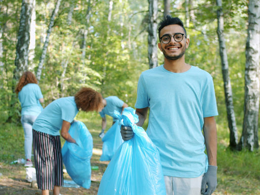 Four people clean up trash in a forest. Person looking at camera is smiling