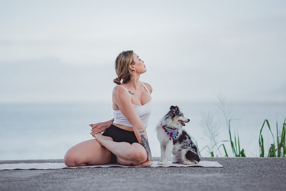 Woman doing yoga with a dog by the ocean, wearing a white top and black shorts. The mood is calm with a serene blue background.
