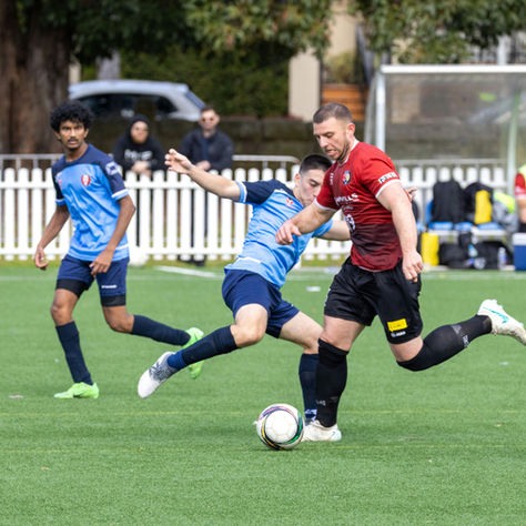 Football player in a red kit shielding the ball under close pressure from a defender in blue, demonstrating ball control and composure skills taught in football coaching sessions in Bournemouth