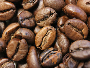 Close-up of glossy roasted coffee beans piled together, showing rich brown tones and textured cracks.