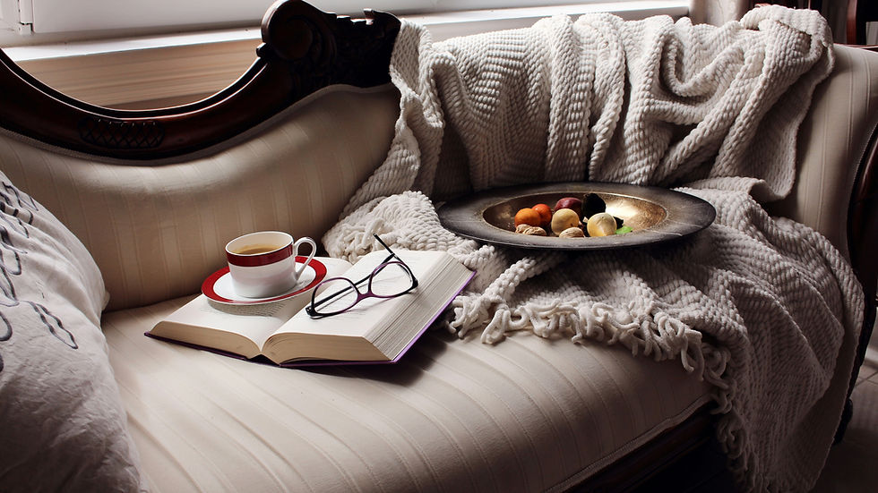 A cozy reading nook featuring a plush couch with a soft, textured throw blanket, a warm cup of tea, and a pair of glasses resting on an open book, inviting moments of empowerment and serenity.
