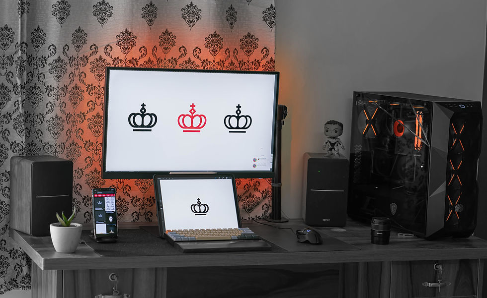 Modern desktop workspace with large monitor, tablet, phone, and RGB PC tower displaying crown logos in a sleek gray room